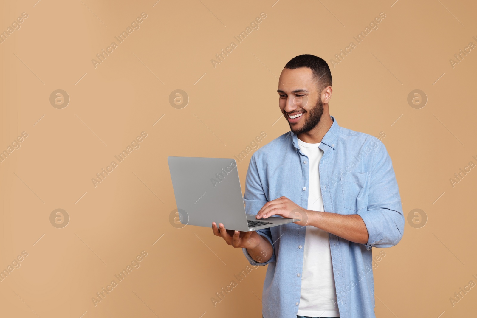 Photo of Smiling young man with laptop working on beige background, space for text