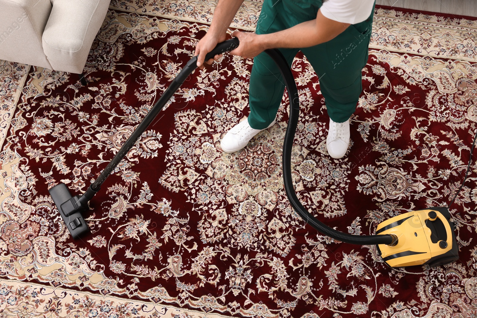 Photo of Dry cleaner's employee hoovering carpet with vacuum cleaner indoors, above view