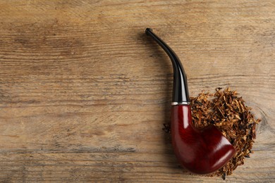 Photo of Smoking pipe with tobacco on wooden table, flat lay. Space for text