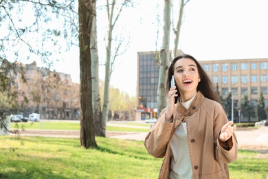 Photo of Young woman talking by phone outdoors on sunny day