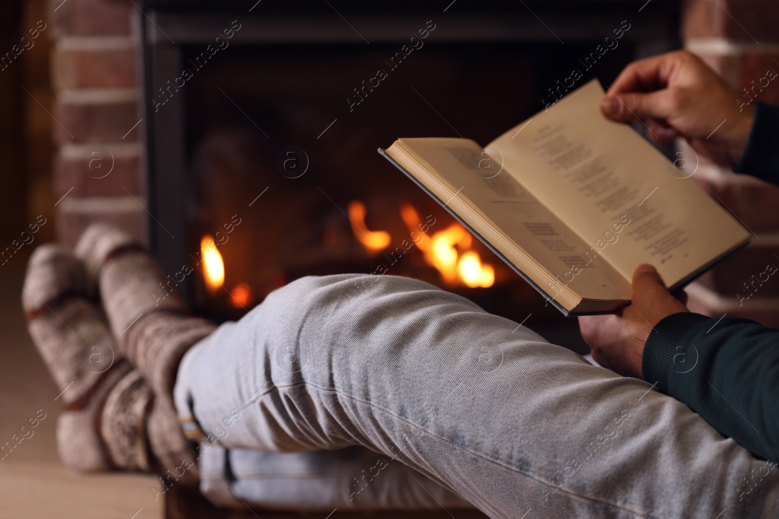 Photo of Man reading book near fireplace at home, closeup