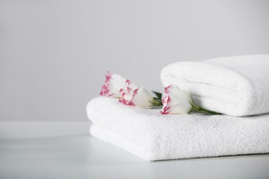 Photo of Folded soft towels with flowers on white table, space for text