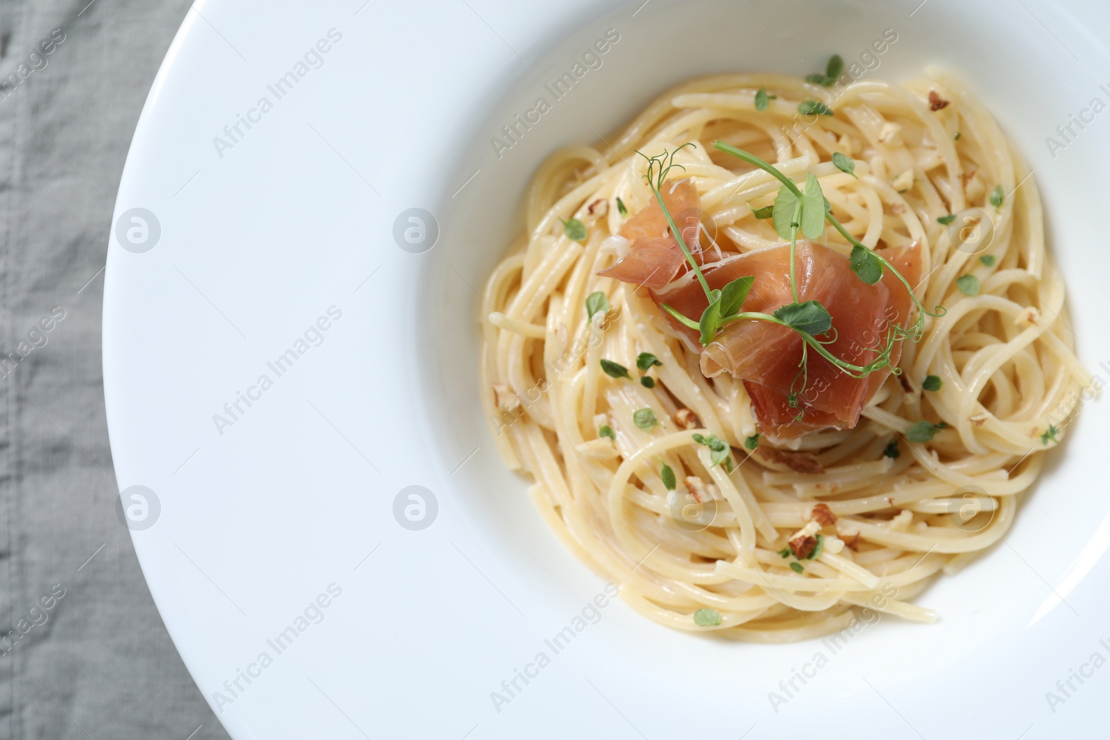 Photo of Tasty spaghetti with prosciutto and microgreens on plate, top view. Exquisite presentation of pasta dish