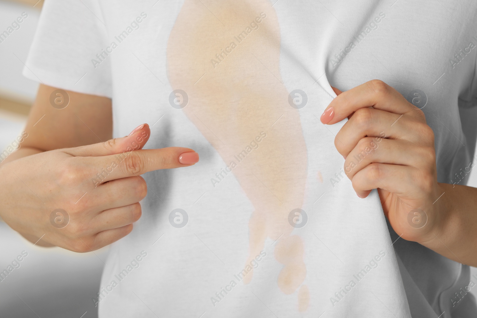 Photo of Woman showing stain from coffee on her shirt indoors, closeup