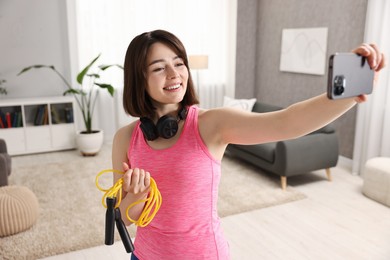 Photo of Happy sports blogger holding skipping rope while streaming online fitness lesson with smartphone at home