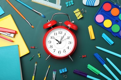 Flat lay composition with alarm clock and different stationery on green chalkboard. School time