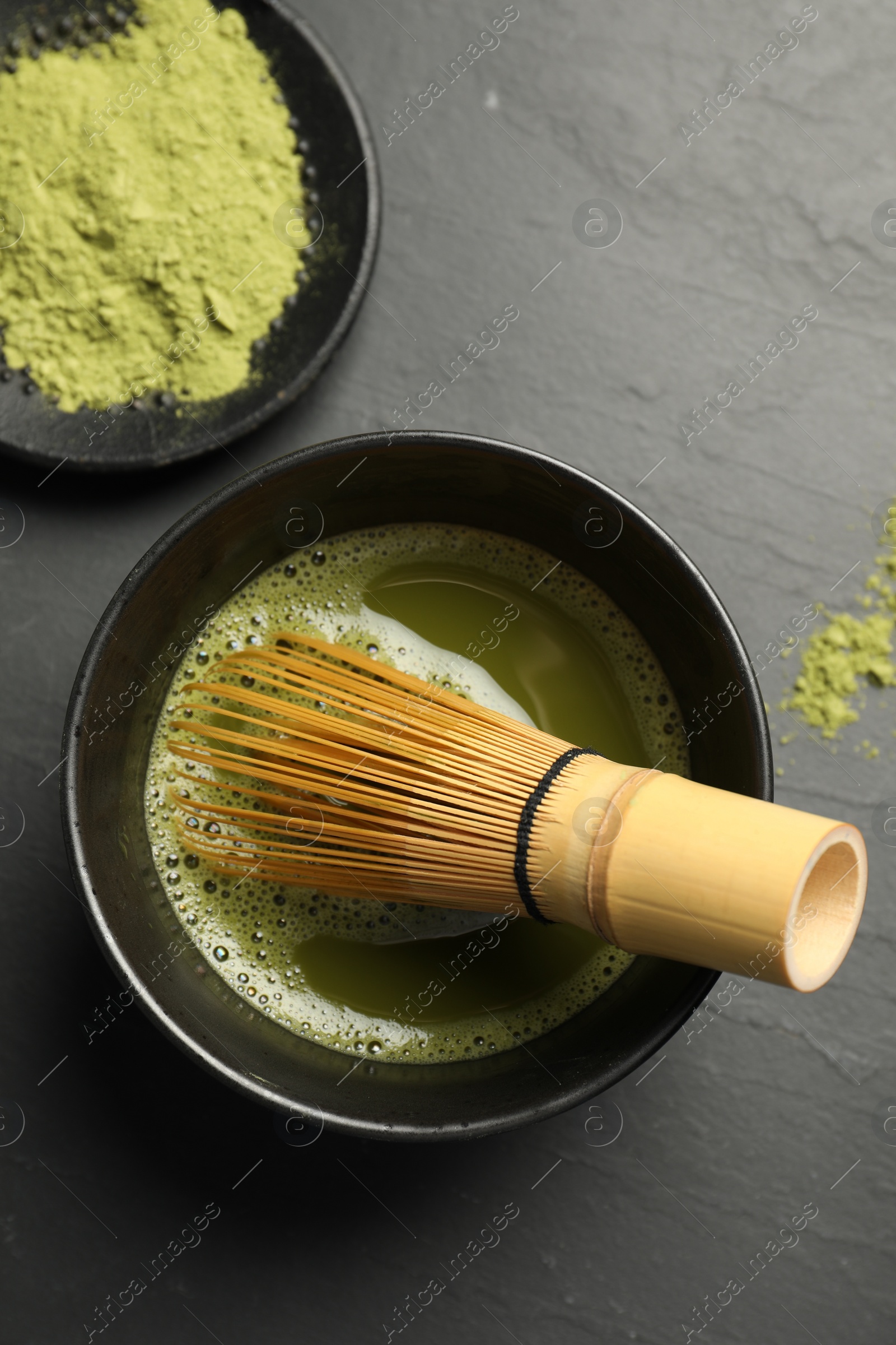 Photo of Cup of fresh matcha tea with bamboo whisk on black table, flat lay