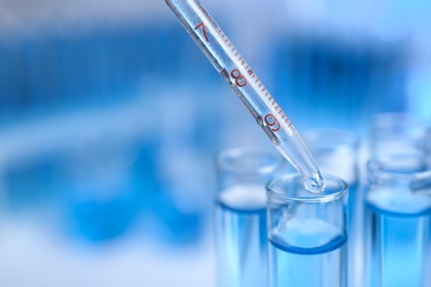 Dripping reagent into test tube with liquid sample on blurred background, closeup and space for text. Laboratory analysis