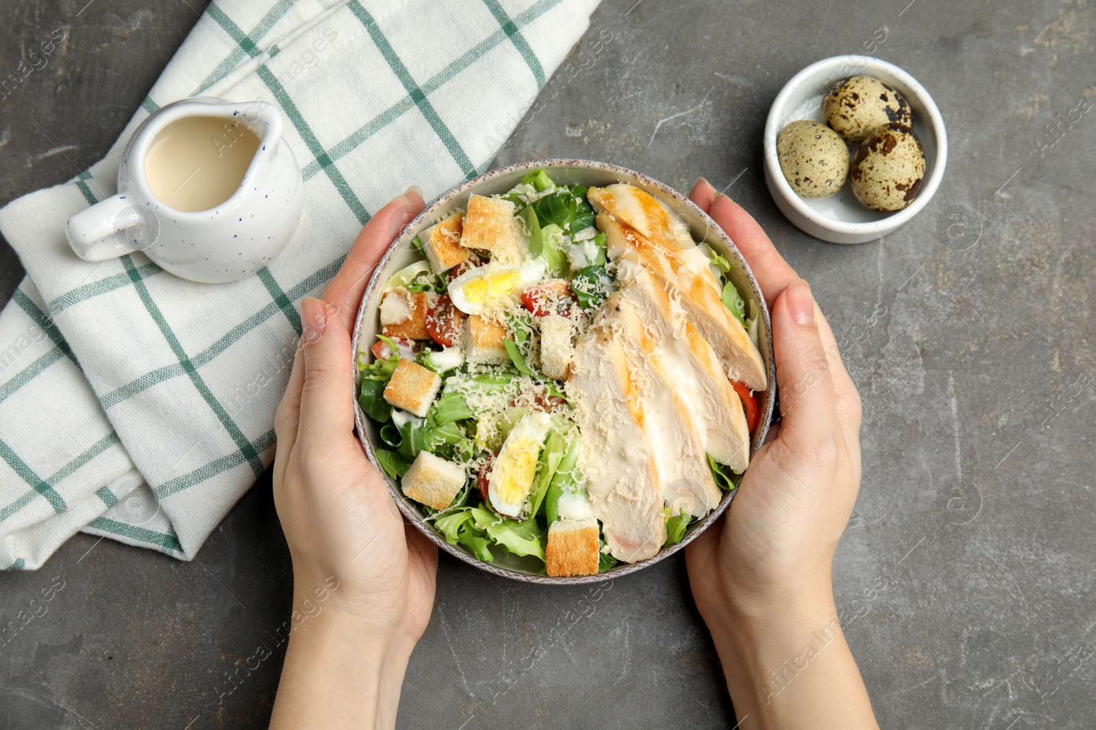 Photo of Woman with bowl of delicious fresh Caesar salad at grey table, top view