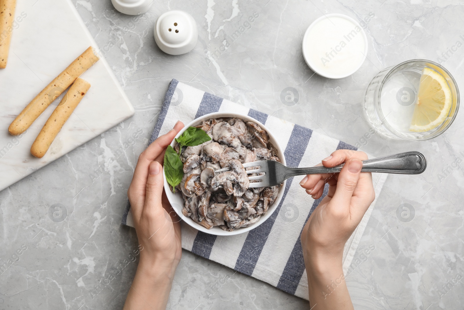 Photo of Woman eating delicious mushrooms at marble table, top view