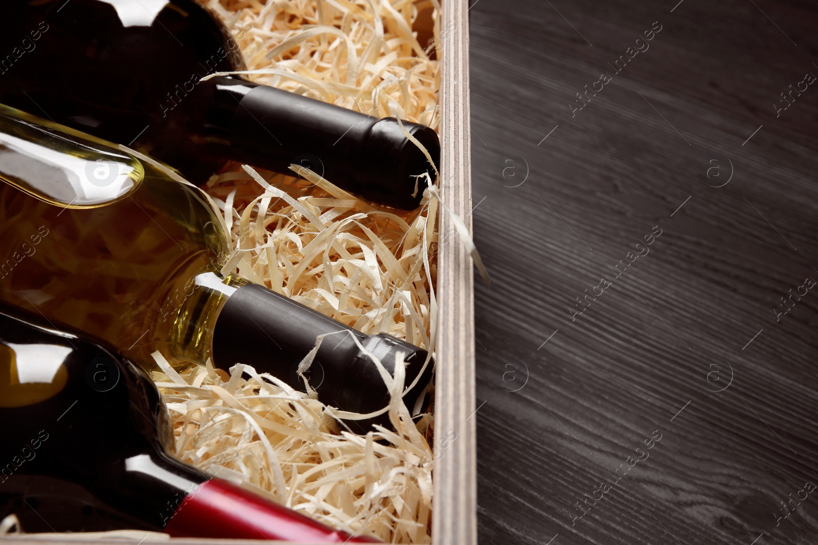 Photo of Wooden crate with bottles of wine on grey table, closeup. Space for text