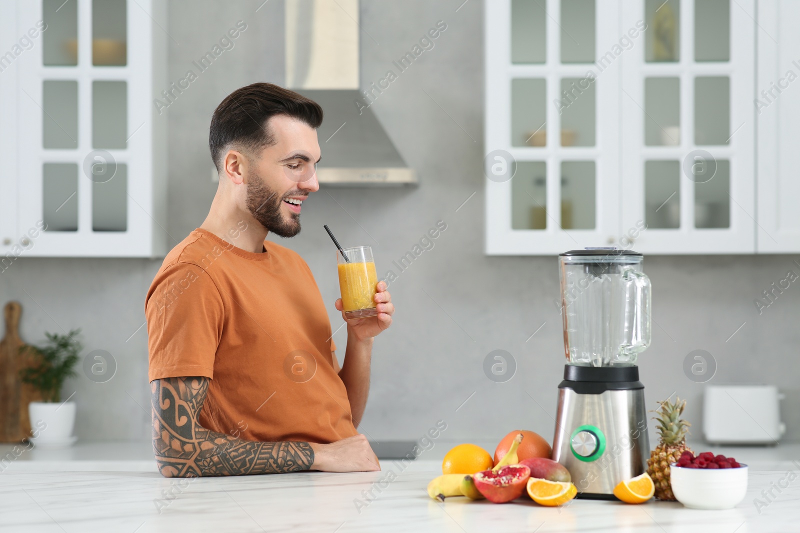 Photo of Handsome man with delicious smoothie at white marble table in kitchen