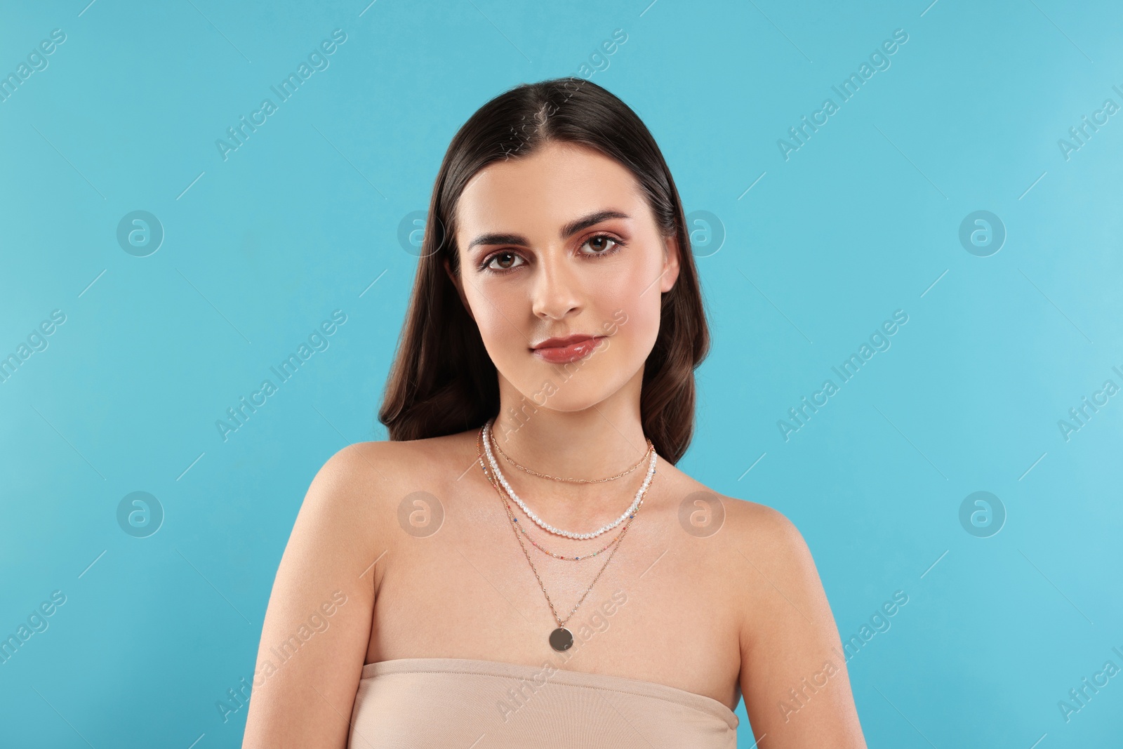 Photo of Beautiful woman with elegant necklaces on light blue background