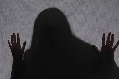 Silhouette of creepy ghost behind grey cloth