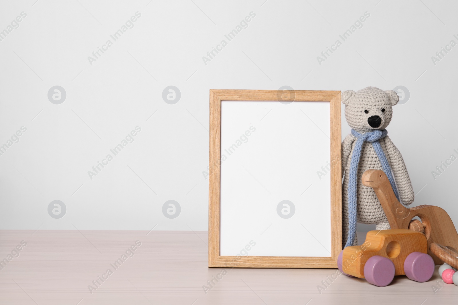 Photo of Empty square frame and different toys on white wooden table, space for text