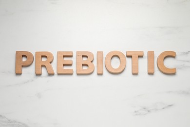 Word Prebiotic made of wooden letters on white marble table, flat lay