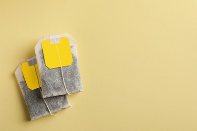 New tea bags with tabs on yellow background, flat lay. Space for text