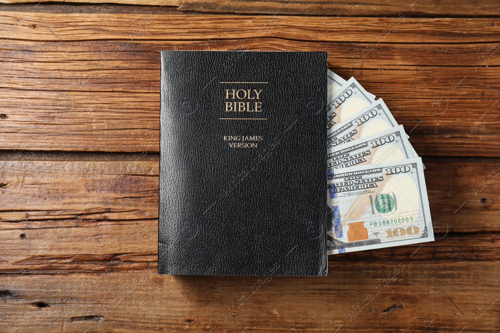 Photo of Holy Bible and money on wooden table, top view
