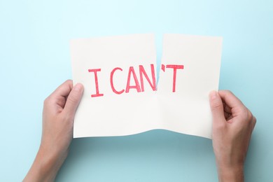 Photo of Motivation concept. Woman making phrase I Can from I Can't by tearing paper on light blue background, top view