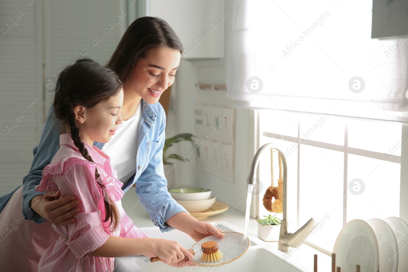 Photo of Mother and daughter washing dishes together in kitchen