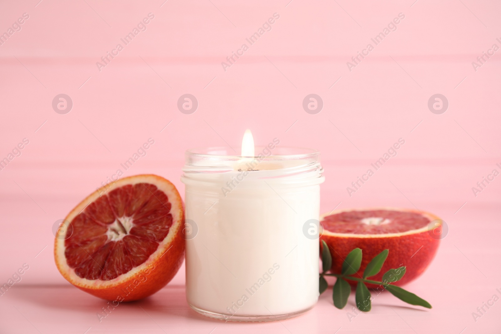 Photo of Scented candle with burning wooden wick and cut grapefruit on pink table