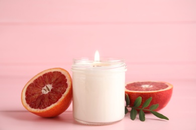 Photo of Scented candle with burning wooden wick and cut grapefruit on pink table