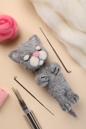 Photo of Felted cat, wool and tools on beige table, flat lay