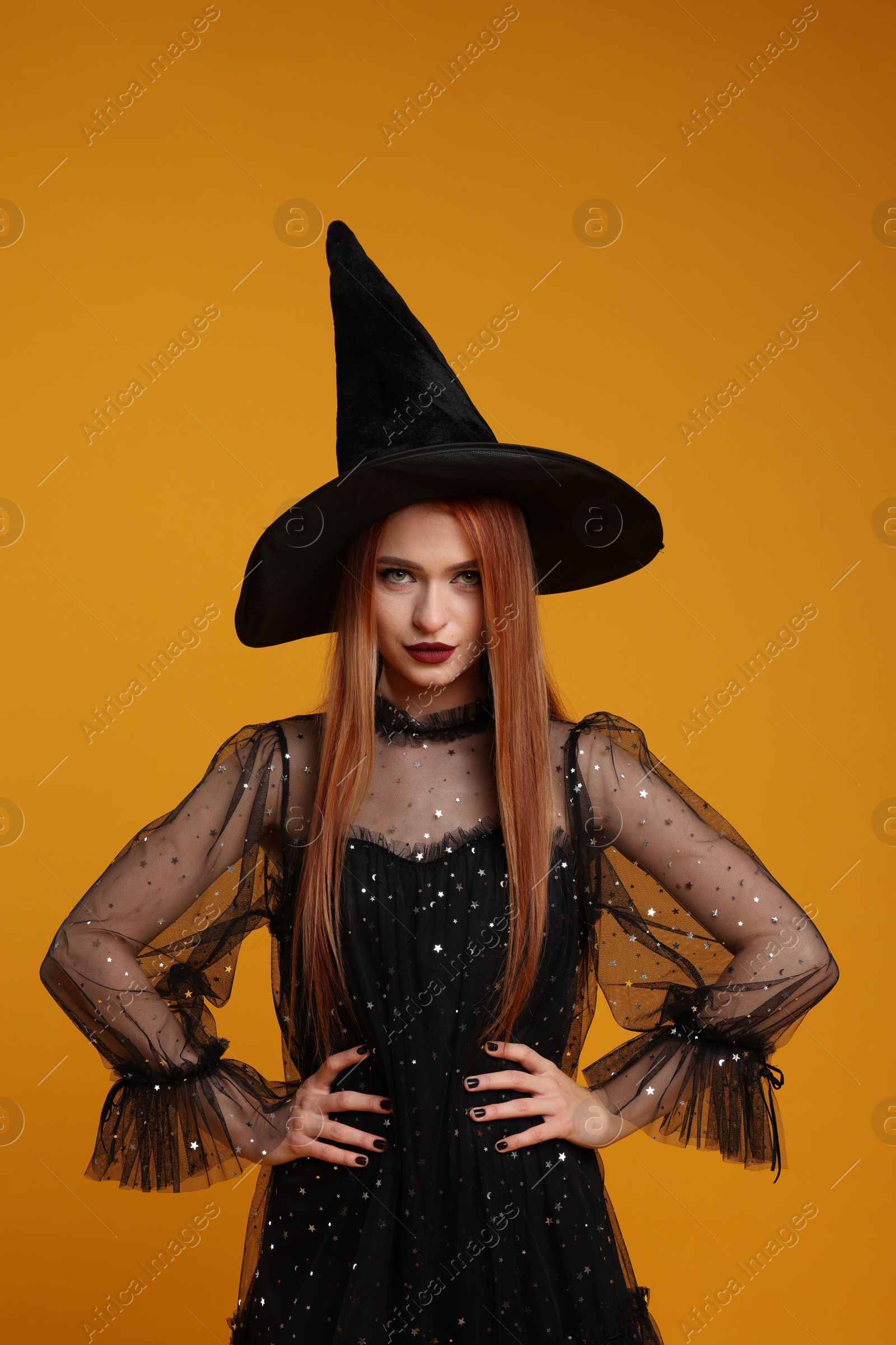 Photo of Young woman in scary witch costume on orange background. Halloween celebration