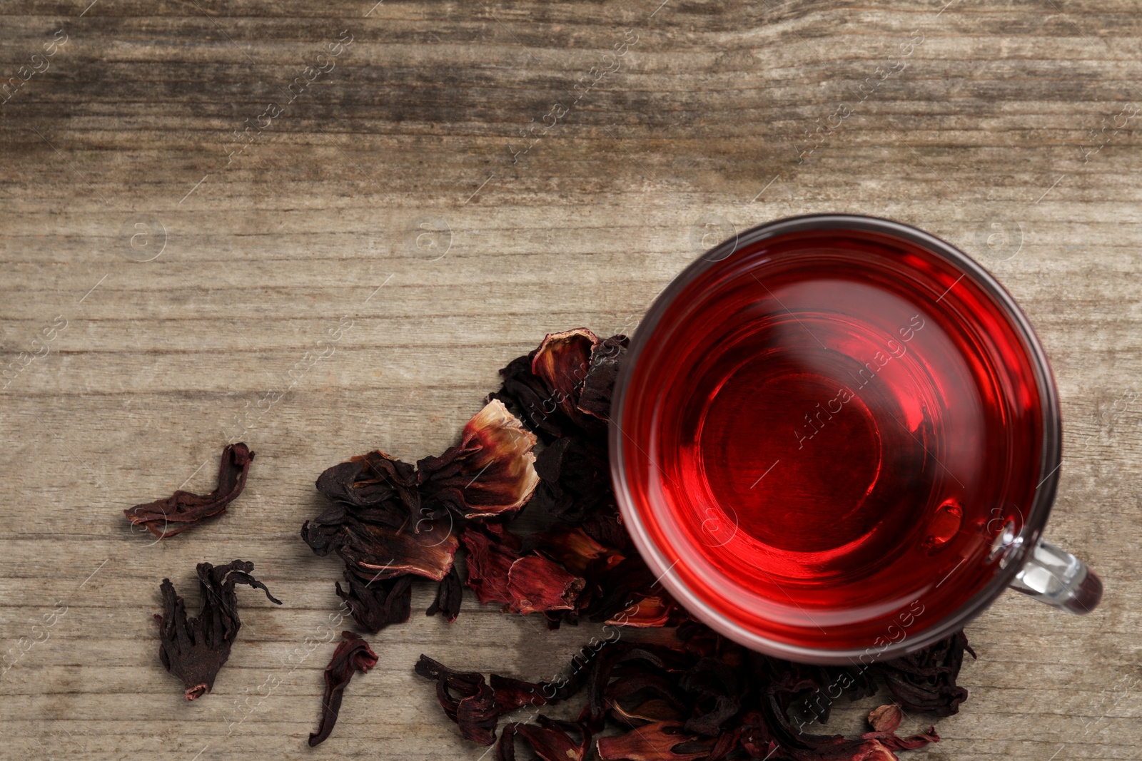 Photo of Cup of fresh hibiscus tea and dry flower leaves on wooden table, flat lay