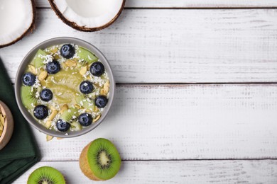 Photo of Bowl of delicious fruit smoothie with fresh blueberries, kiwi slices and coconut flakes on white wooden table, flat lay. Space for text