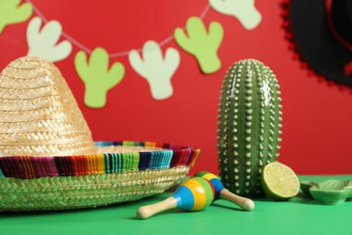 Composition with Mexican sombrero hat and maracas on green table, closeup