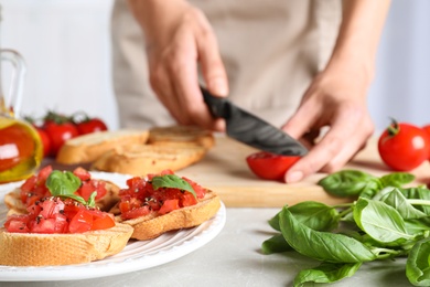 Photo of Woman cutting tomato at light grey table, focus on tasty bruschetta