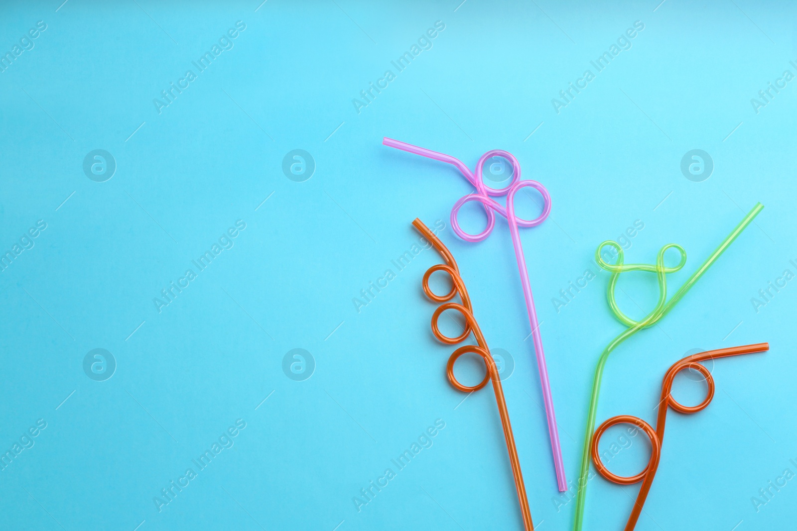 Photo of Colorful plastic drinking straws on light blue background, flat lay. Space for text