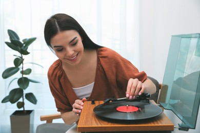 Photo of Happy young woman using turntable at home
