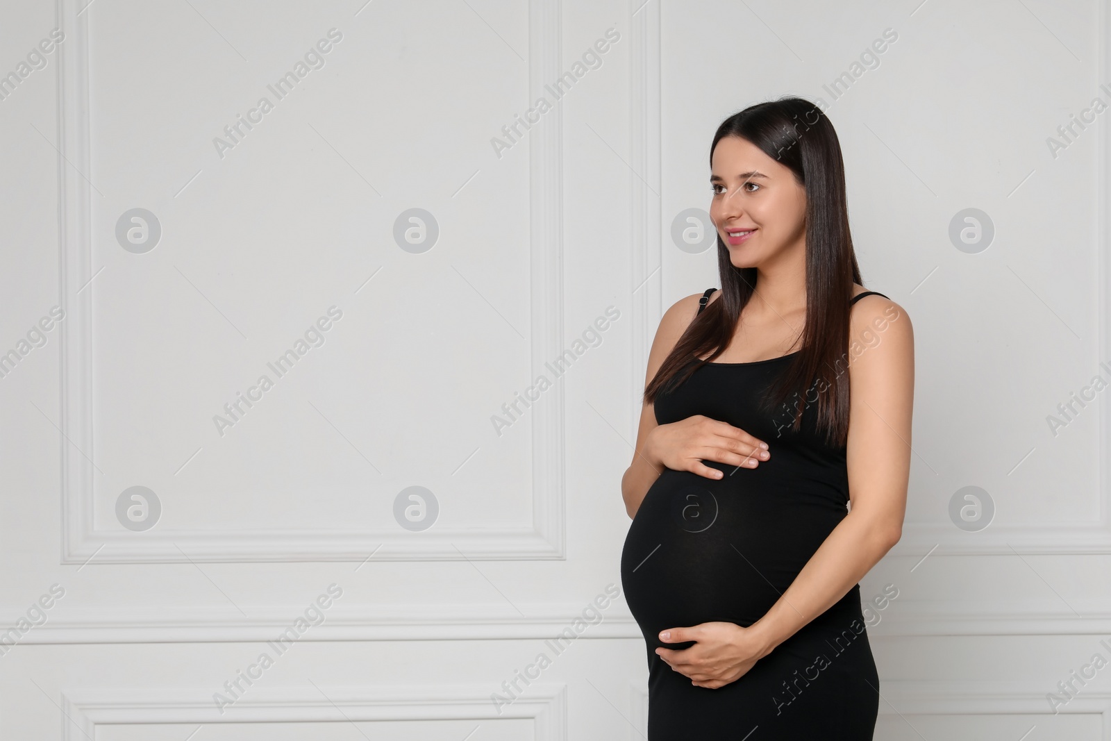 Photo of Beautiful pregnant woman in black dress near light grey wall, space for text