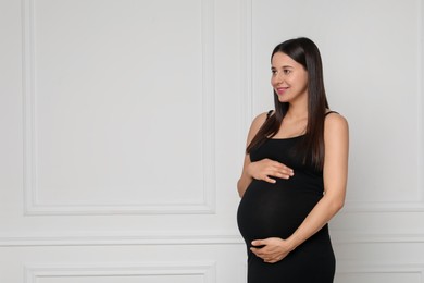 Beautiful pregnant woman in black dress near light grey wall, space for text