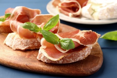 Photo of Tasty sandwiches with cured ham and basil leaves on blue wooden table, closeup