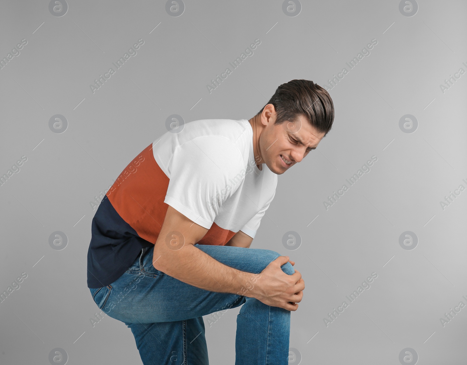 Photo of Young man suffering from knee pain on grey background