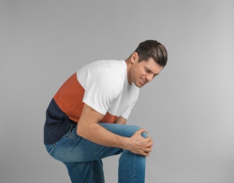 Photo of Young man suffering from knee pain on grey background
