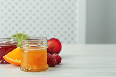 Photo of Jars of different jams and ingredients on white wooden table, space for text