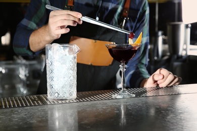 Barman decorating alcoholic cocktail at counter in pub, closeup