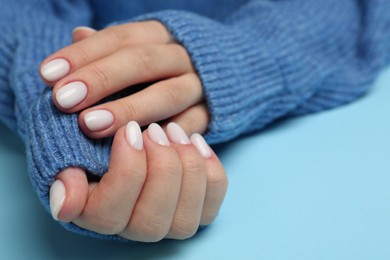 Woman showing her manicured hands with white nail polish on light blue background, closeup. Space for text