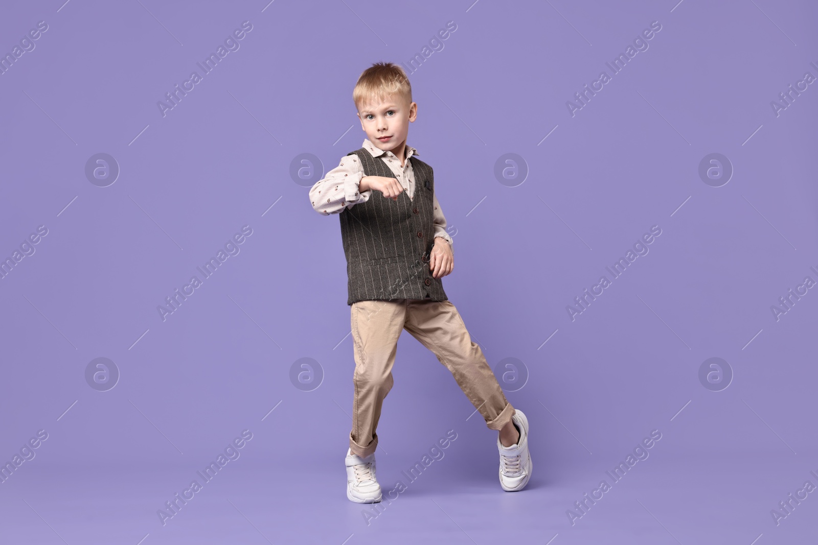 Photo of Happy little boy dancing on violet background