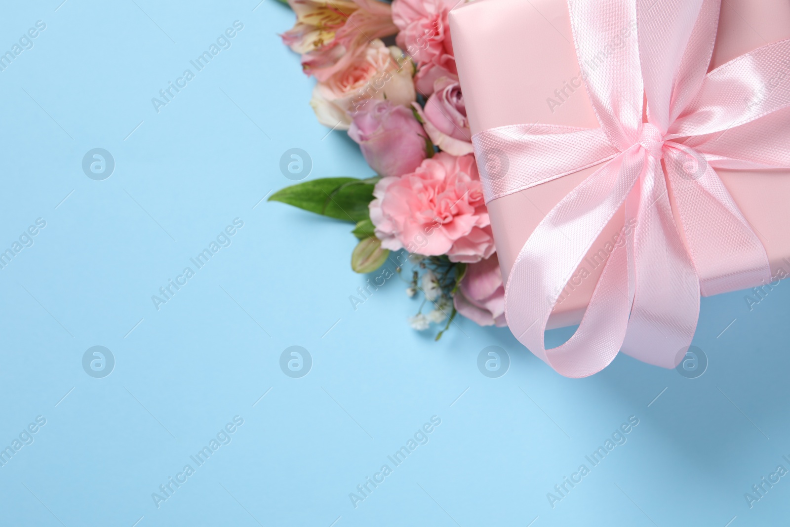 Photo of Gift box and beautiful flowers on light blue background, flat lay. Space for text