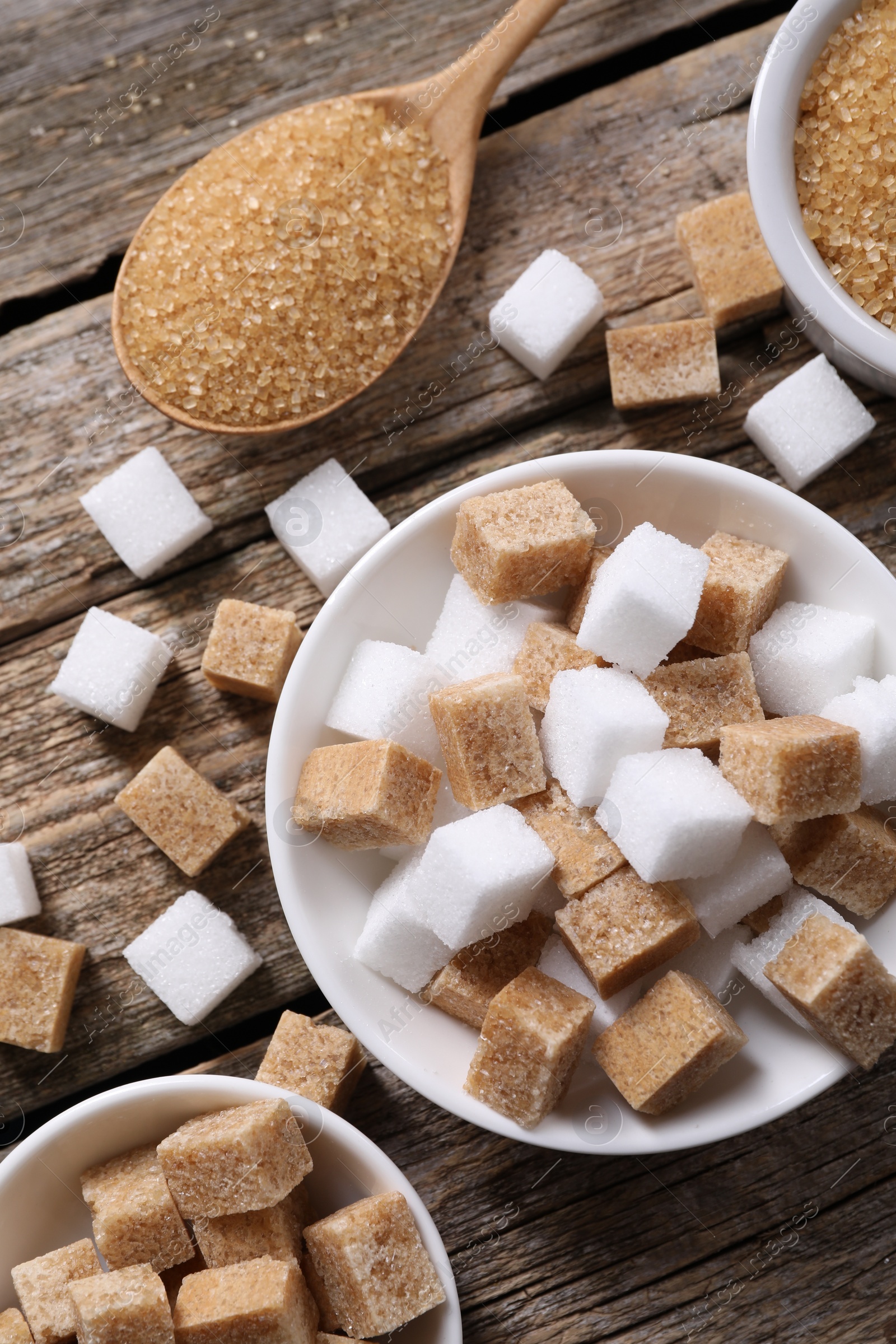 Photo of Different types of sugar in bowls and spoon on wooden table, flat lay