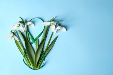 Photo of Beautiful snowdrops and number 8 made of ribbon on light blue background, flat lay. Space for text