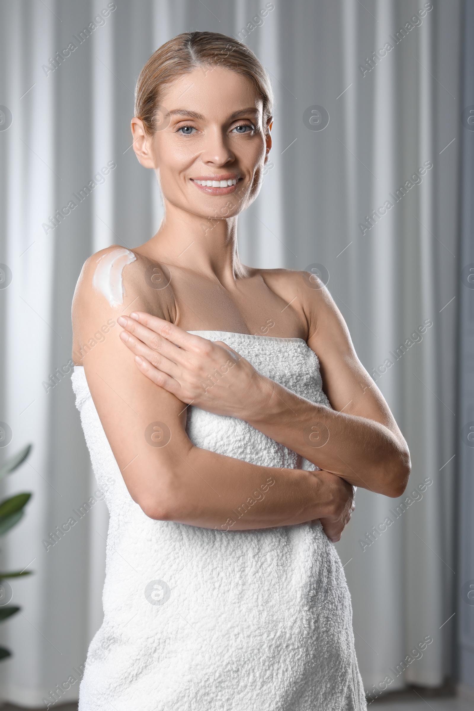 Photo of Happy woman applying body cream onto shoulder indoors
