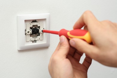 Professional electrician with screwdriver repairing light switch, closeup