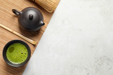Photo of Cup of fresh matcha tea, bamboo whisk, spoon and teapot on light grey table, top view. Space for text