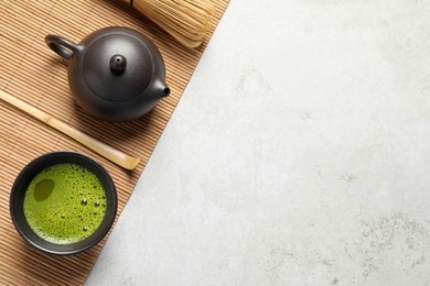 Cup of fresh matcha tea, bamboo whisk, spoon and teapot on light grey table, top view. Space for text